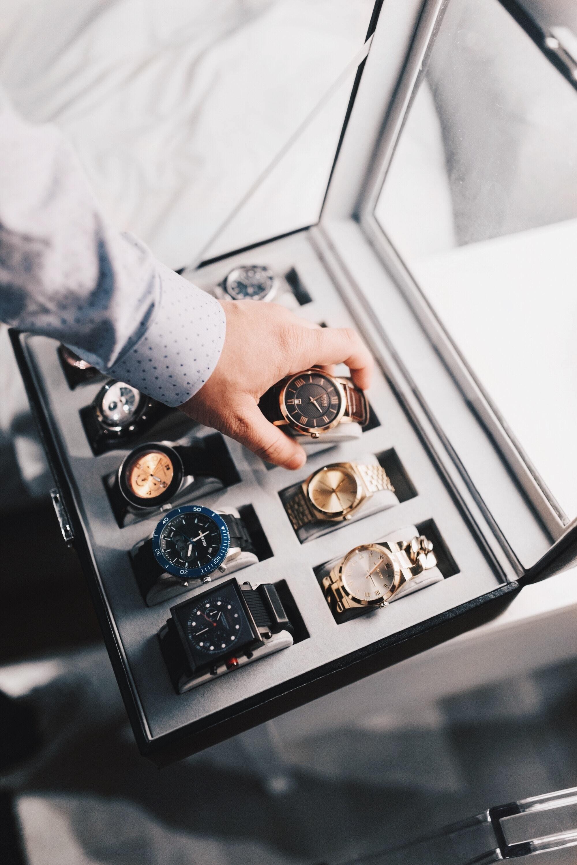 a man's hand grabbing a watch from watch cabinet